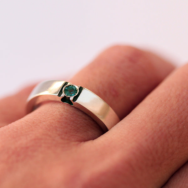 White gold paw print ring worn on hand featuring green birthstone set in black enamel negative space design for animal lover jewelry.