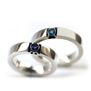 Matching white gold couple rings with amethyst and blue topaz birthstones showing hidden paw print design revealed when rings align.