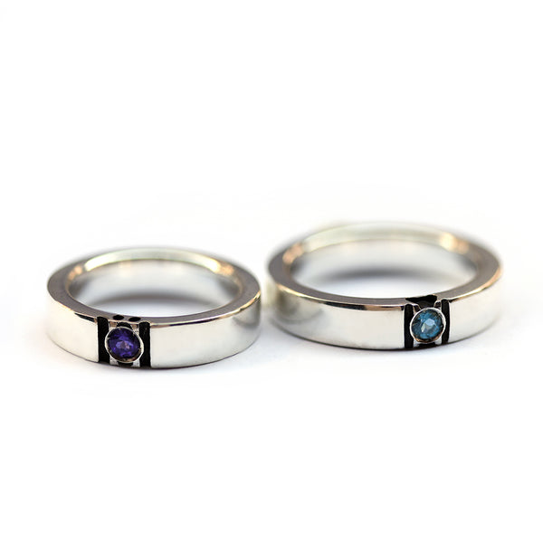 Pair of paw print wedding rings lying flat showing gemstone placement and subtle hidden paw negative space couple ring structure.