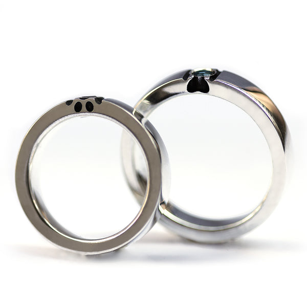 Interior and side view of matching couple bands showing paw print cutout and gemstone setting within thick white gold wedding rings.