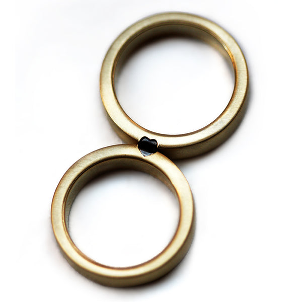 Matching couple wedding rings with black diamond heart detail, handcrafted 18K gold bands with brushed matte finish, personalized wedding jewelry