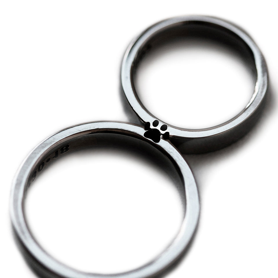 Matching black rhodium couple rings aligned together revealing full hidden paw print silhouette created in negative space between both bands.