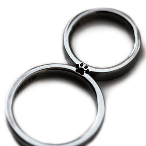 Matching black rhodium couple rings aligned together revealing full hidden paw print silhouette created in negative space between both bands.
