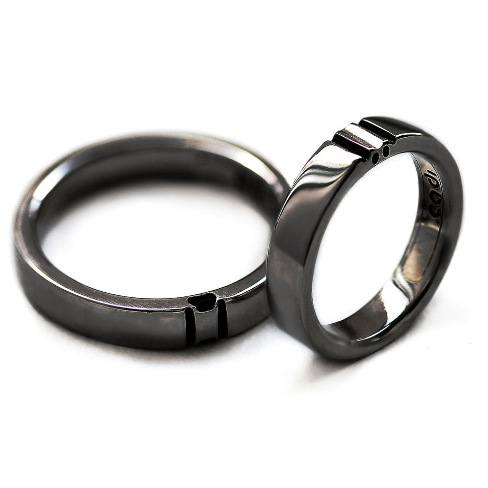 Matching black rhodium couple rings aligned together revealing full hidden paw print silhouette created in negative space between both bands.
