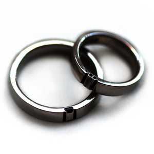 Close up of black rhodium plated couple rings touching side by side highlighting hidden paw print negative space relationship ring design.