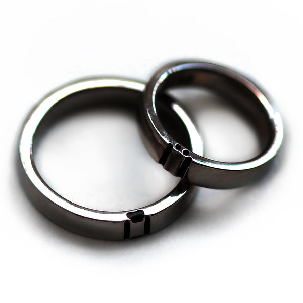 Close up of black rhodium plated couple rings touching side by side highlighting hidden paw print negative space relationship ring design.