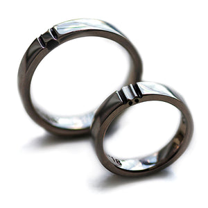 Matching black rhodium wedding bands standing upright showing polished dark finish and divided paw print motif across both connected rings.