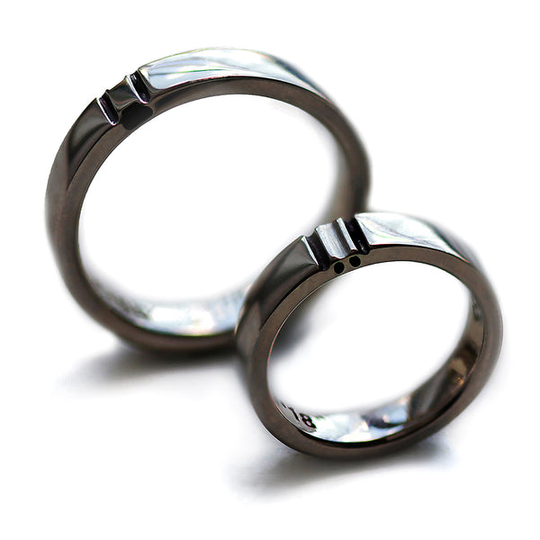 Matching black rhodium wedding bands standing upright showing polished dark finish and divided paw print motif across both connected rings.