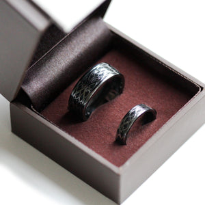 Matching black rhodium Celtic wedding bands displayed in ring box with braided silver pattern and black hot enamel inlay