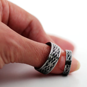 Black rhodium plated Celtic braided wedding bands shown worn on fingers highlighting silver scroll pattern and black hot enamel