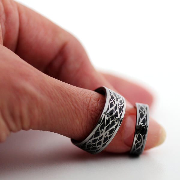 Black rhodium plated Celtic braided wedding bands shown worn on fingers highlighting silver scroll pattern and black hot enamel
