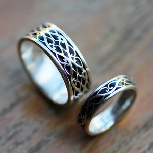 Angled close up of Celtic braided his and hers sterling silver wedding bands with black hot enamel background