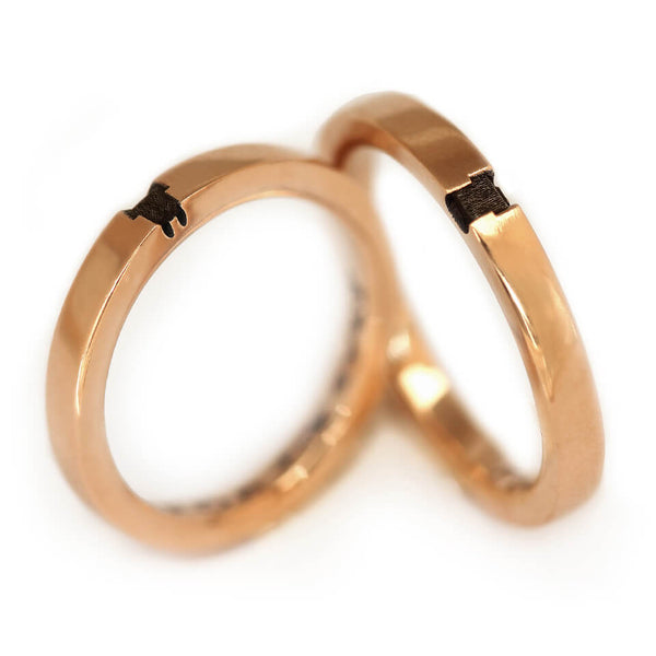 Close angled view of the rose gold couple rings highlighting sections of the fox and bunny engraving flowing across each band as part of the dual spirit animal design.