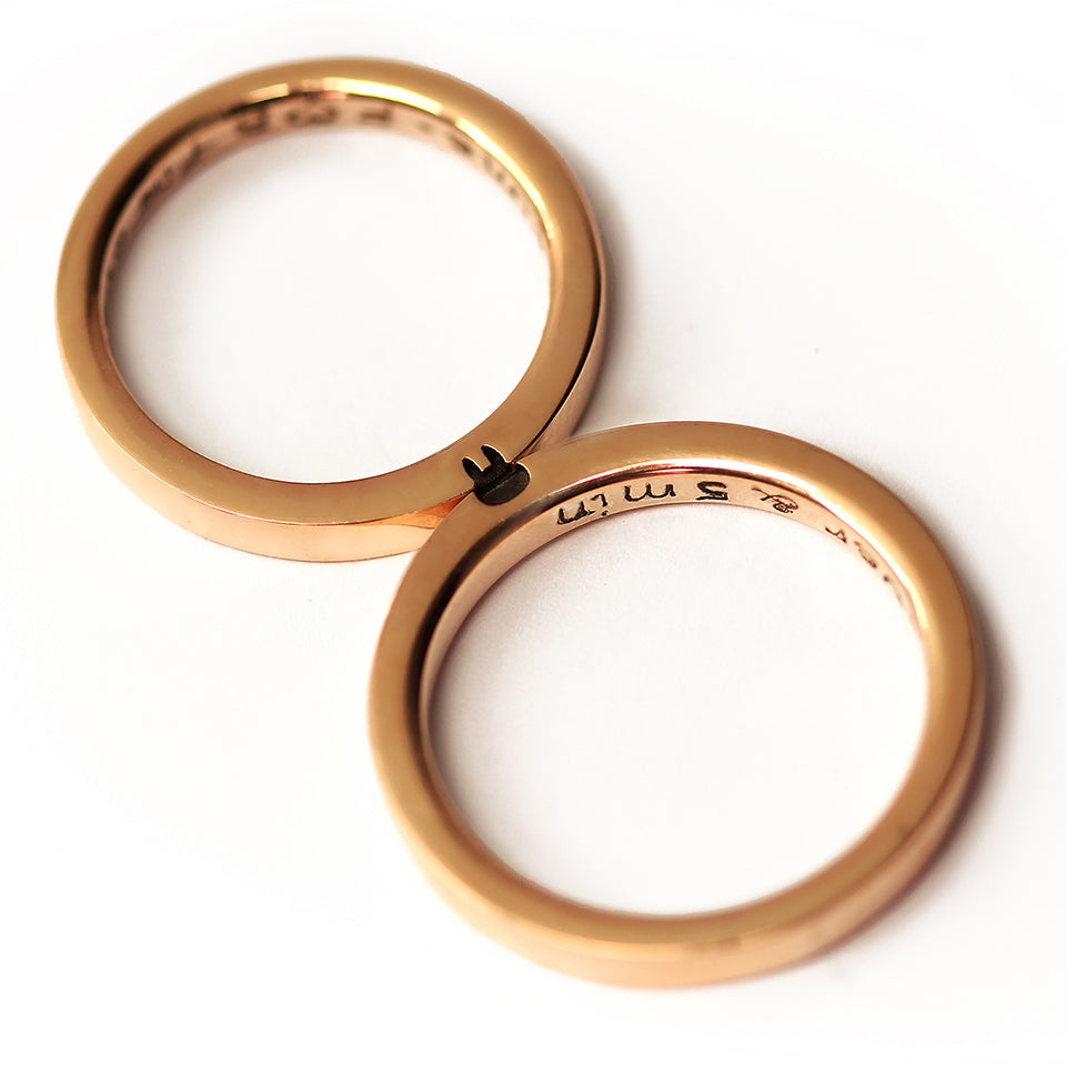 Two 18K rose gold couple rings placed side by side showing the engraved fox silhouette across the outer surface of both matching bands.