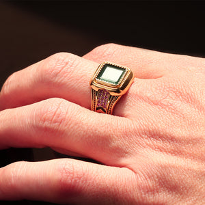 Square emerald statement ring worn on hand with ruby side accents, handcrafted yellow gold band, black hot enamel chevron pattern and filigree engraving