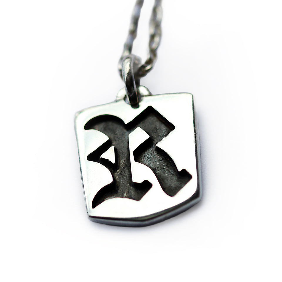 Gothic initial tag pendant necklace in polished sterling silver featuring cutout Old English letter design with darkened background detail