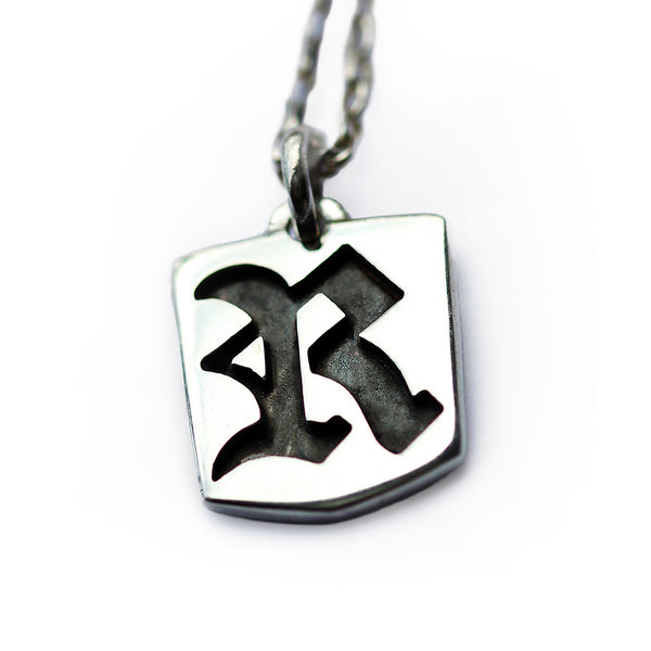 Gothic initial tag pendant necklace in polished sterling silver featuring cutout Old English letter design with darkened background detail