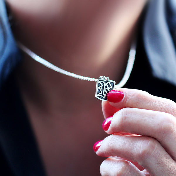 Close-up of a silver necklace with a gothic initial letter tag pendant held by a hand .