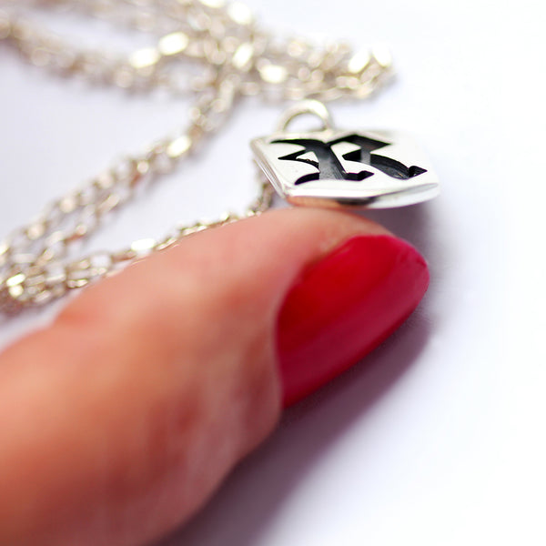 Close up of sterling silver gothic initial tag necklace held by hand showing detailed Old English letter cutout and polished finish