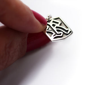 Silver gothic letter tag pendant held by a hand on a white background