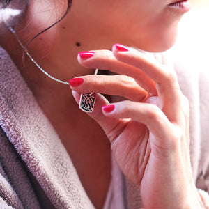 Close-up of a person wearing a necklace with a gothic initial letter tag pendant, held by their hand.