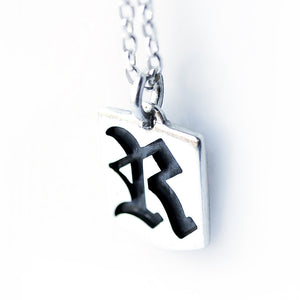 Side angle close up of sterling silver gothic initial tag pendant showing dimensional letter cutout craftsmanship and chain connection