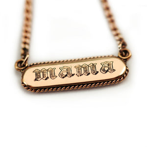 18k gold necklace with 'mama' tag in gothic font and filigree around it, pendant on a white back