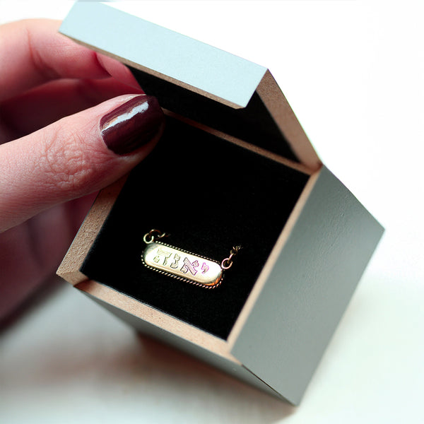18k Gold necklace with a tag name pendant in an open jewelry box held by a hand.