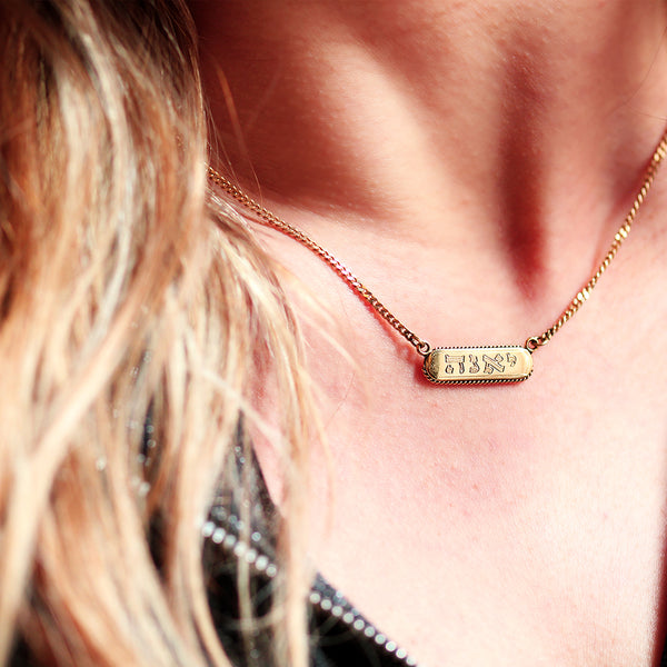 Gold necklace with a bar name tag engraved pendant worn by a blonde women