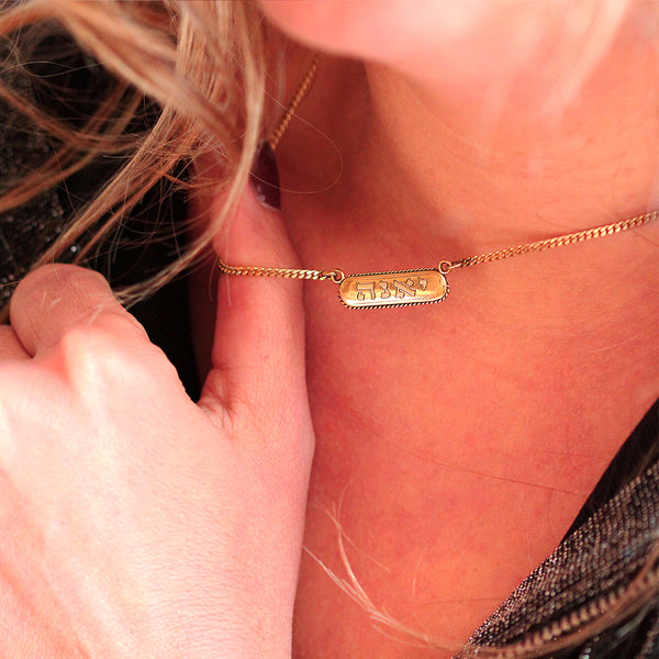 Close-up of a gold necklace with a rectangular pendant tag name engraved 