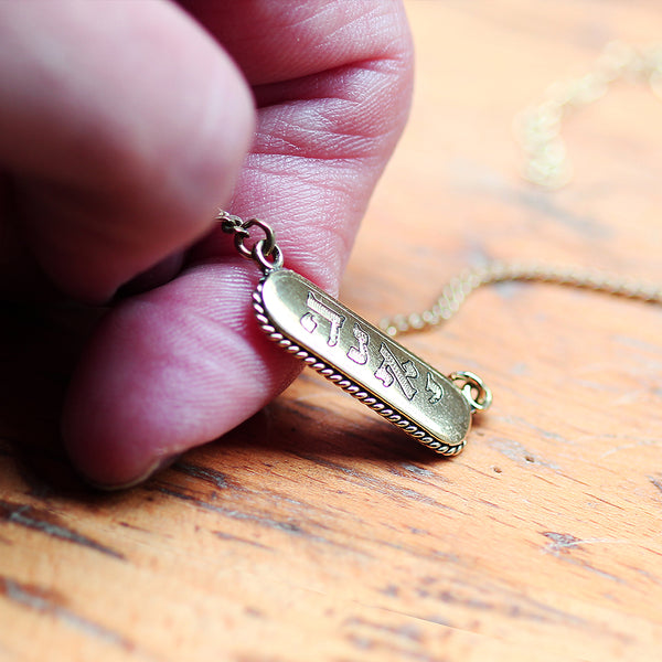 Gold necklace with an engraved pendant held by a hand 