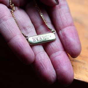 Gold necklace with a bar tag name engraved pendant held in a hand 