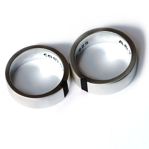 Two silver or 18K white gold couple rings with black hot enamel inlay, positioned to show the unique interior  personal engravings.