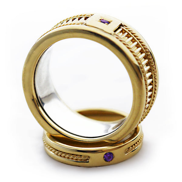 Close up of handcrafted yellow gold wedding ring highlighting purple sapphire accent, decorative filigree engraving and textured vintage band finish