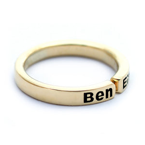 Close up angled view of personalized mother ring with children’s names, handcrafted 18K solid gold open band with blackened engraved lettering