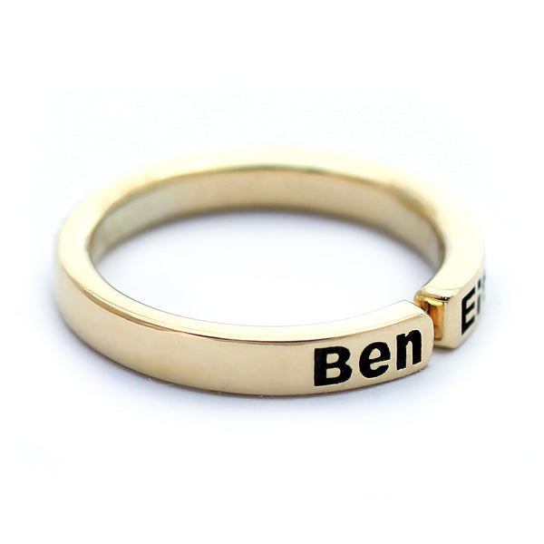 Close up angled view of personalized mother ring with children’s names, handcrafted 18K solid gold open band with blackened engraved lettering