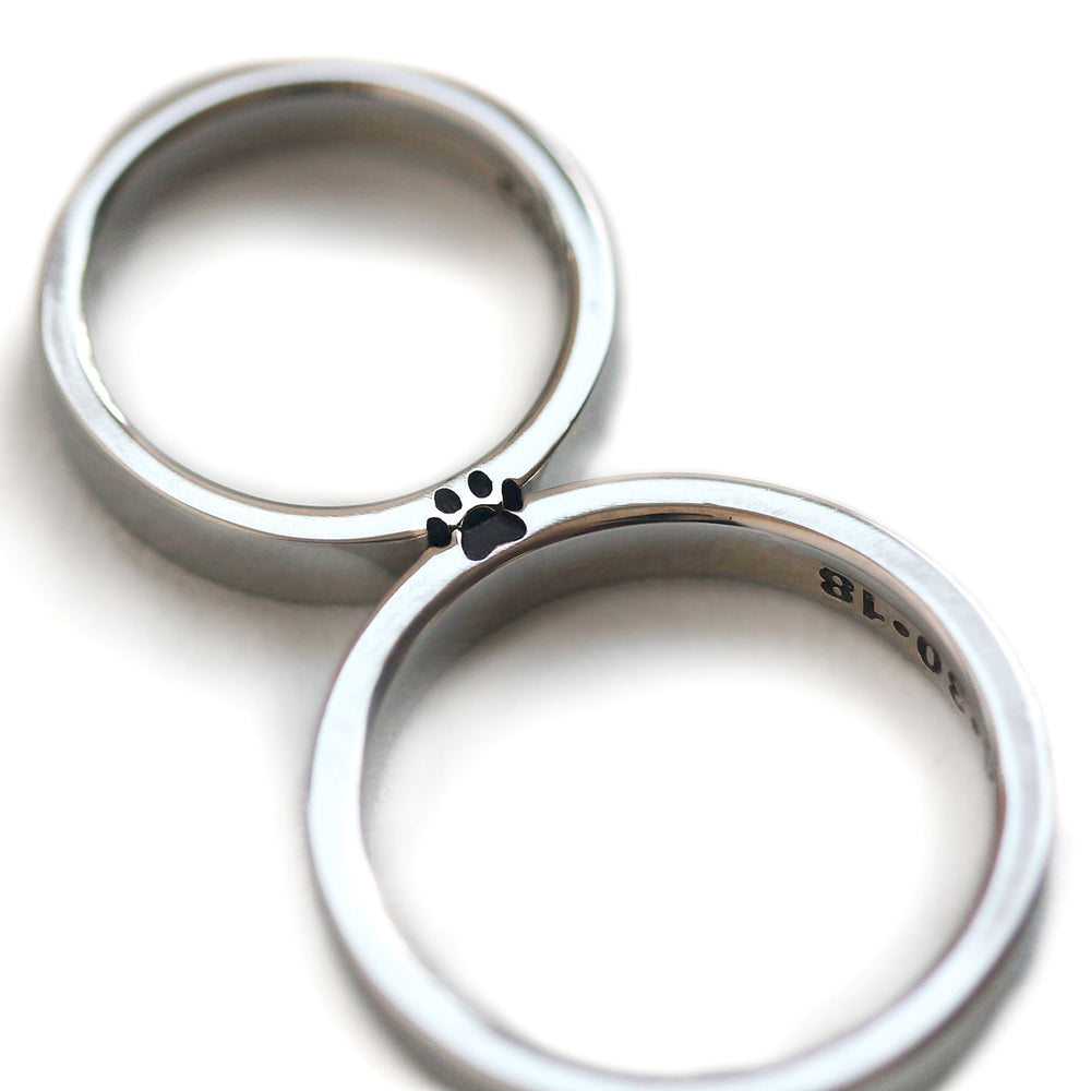 White gold couple rings positioned together revealing a hidden paw print formed in negative space where the two bands meet.