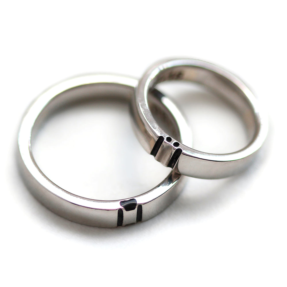 White gold couple rings positioned together revealing a hidden paw print formed in negative space where the two bands meet.