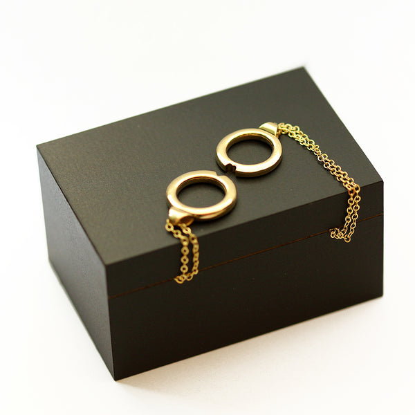 Matching couples necklace with two interlocking yellow gold circle pendants placed on jewelry box, symbolic design that forms a heart when connected and can be shared between partners