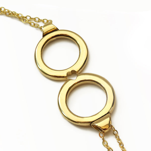 Matching couples necklace with two interlocking yellow gold circle pendants designed to form a heart shape when connected and can be worn together or shared between partners