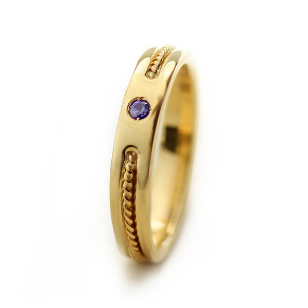 Thin 18k yellow gold wedding band featuring braided rope filigree detail and bezel set purple sapphire, elegant minimalist bridal stacking ring
