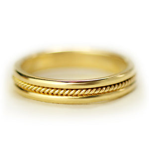 Close up of thin 18k gold sapphire wedding band featuring bezel set purple sapphire and decorative rope filigree pattern
