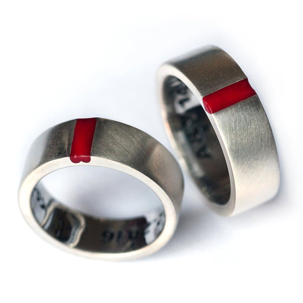 Two 18K white gold wedding rings with a matte brushed finish, featuring a vertical red enamel stripe on the face of each band.