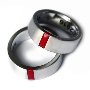 A stacked view of 18k white gold couple rings showing the red enamel inlay and personalized interior engraving, representing a shared partnership identity.