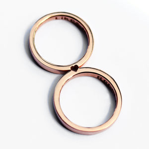 Rose gold hidden heart couple rings aligned to reveal small heart cutout, minimalist matching wedding or promise rings.