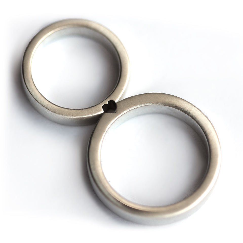 Silver hidden heart couple rings aligned together revealing subtle heart cut design, minimalist matching wedding bands