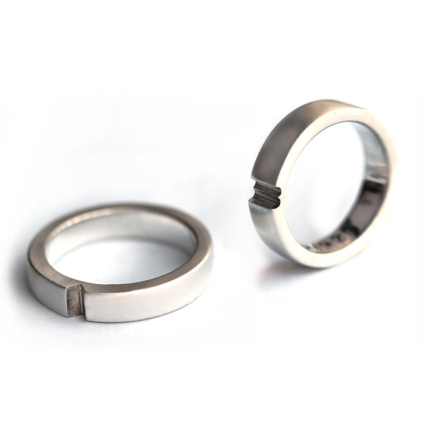 Two silver hidden heart rings separated showing interlocking notch design, contemporary his and hers wedding bands