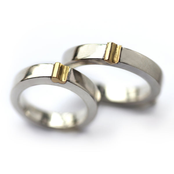Close-up of matching magnetic wedding bands, white gold with yellow gold connector detail, two-tone couple ring set