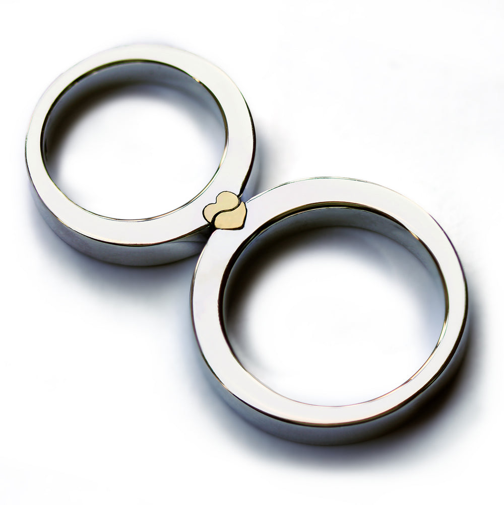 
Magnetic couple rings placed together forming a solid yellow gold heart, two tone wedding bands combining polished white gold with interlocking heart design revealed when the rings connect.