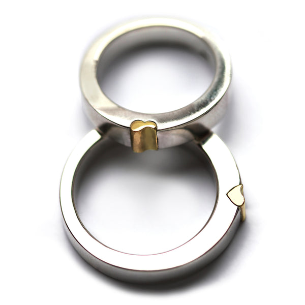 Interlocking magnetic wedding rings displayed vertically, highlighting the yellow gold heart connector and polished white gold bands that form a hidden heart when joined together.
